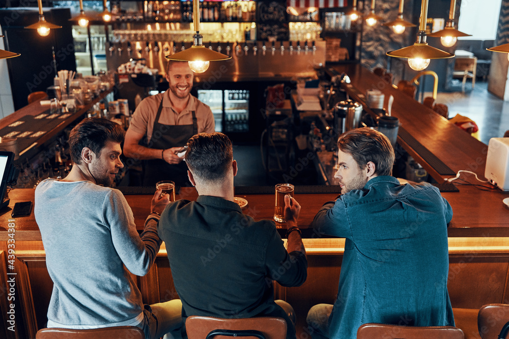 Top view of relaxed young men in casual clothing drinking beer while sitting in the pub Top view of relaxed young men in casual clothing drinking beer while sitting in the pub