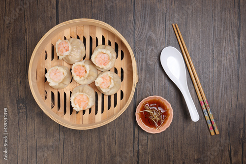 Prawn shrimp shaomai dim sum dumpling in bamboo steamer sauce chopsticks soup soon on rustic wood background photo