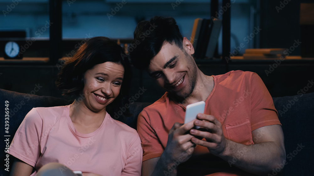 cheerful man and woman looking at smartphone and smiling in modern living room. cheerful man and woman looking at smartphone and smiling in modern living room.