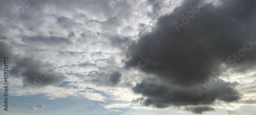 Cumulus clouds float across the invisible sky. Large, wide clouds of various shapes and shades of gray from black to white cover almost all of the blue sky.