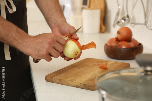 Man peeling onion at kitchen counter, closeup. Preparing vegetable