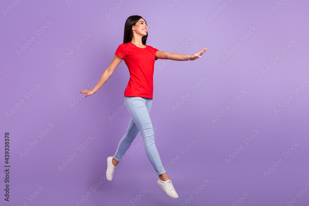 Full length photo of sweet adorable woman dressed red t-shirt jumping high looking empty space smiling isolated purple color background