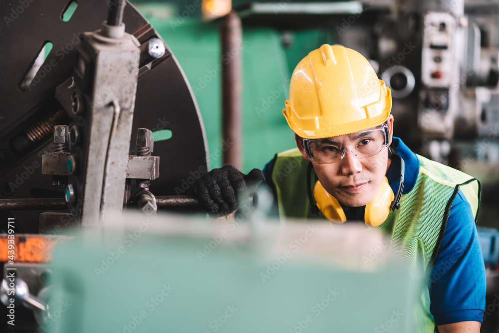 Work at factory.Asian worker man working in safety work wear with yellow helmet and glasses l ear muff using equipment.Close up male technician asia in factory workshop industry machine professional Work at factory.Asian worker man working in safety work wear with yellow helmet and glasses l ear muff using equipment.Close up male technician asia in factory workshop industry machine professional