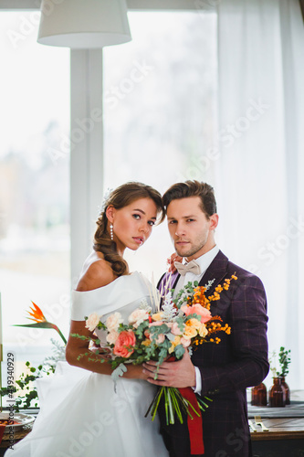Beautiful and stylish couple of newlyweds are posing with bridal bouquet
