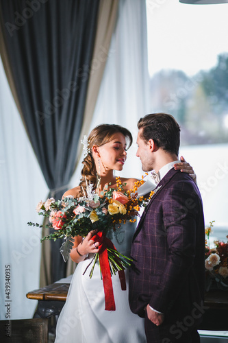 Beautiful and stylish couple of newlyweds are posing with bridal bouquet