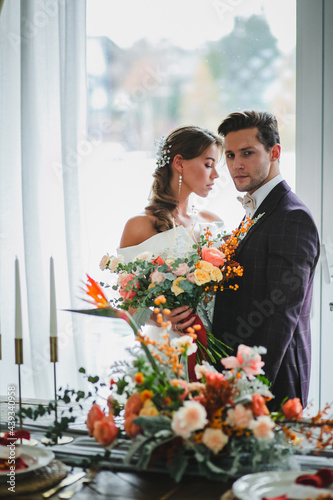 Beautiful and stylish couple of newlyweds are posing with bridal bouquet