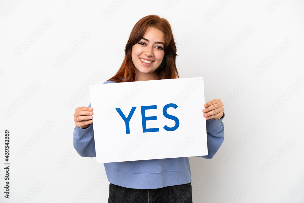 Young redhead woman isolated on white background holding a placard with text YES with happy expression Young redhead woman isolated on white background holding a placard with text YES with happy expression
