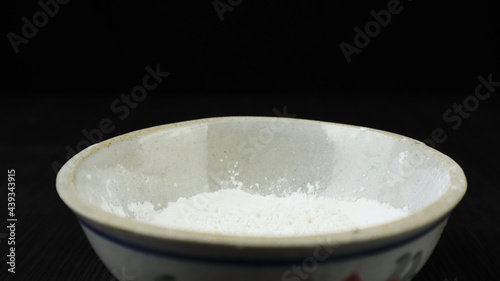 white flour and ceramic bowl on wooden table and black background