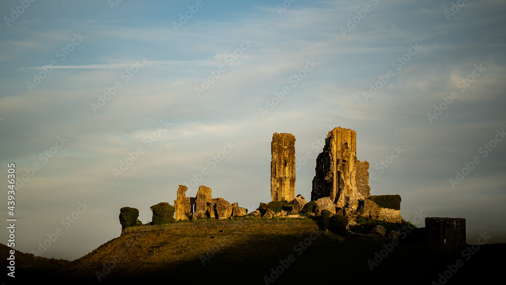 Sunset on the background of Corfe Castle ruins Dorset United Kingdom ,partially covered with shadow on blu cloudy sky ,looks beautiful 