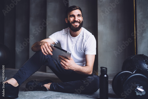 Cheerful caucasian male in activewear using modern digital tablet for blogging and share media content online, smiling sportsman checking results and gals for slimming and keeping perfect body shape