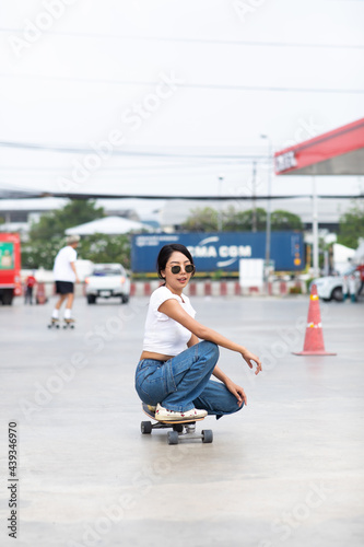 Asian young woman playing surfskate or skate board in gas station urban city outdoor. Extream sports