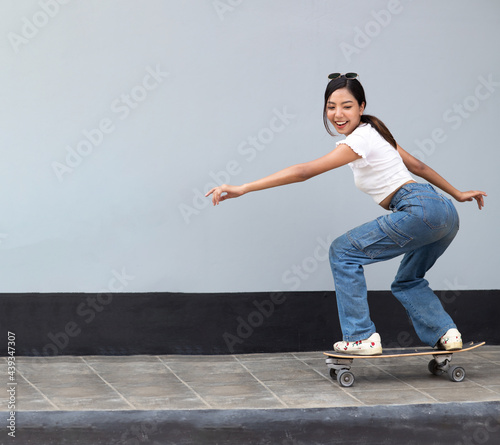 Fototapeta Naklejka Na Ścianę i Meble -  Asian young woman playing surfskate or skate board isolated on gray background at urban city outdoor. Extream sports