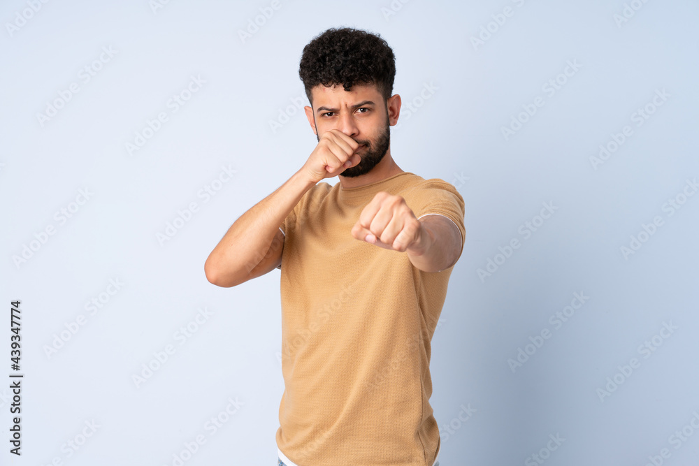 Young Moroccan man isolated on blue background with fighting gesture Young Moroccan man isolated on blue background with fighting gesture
