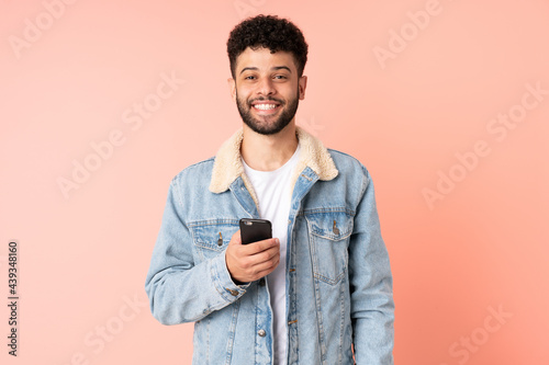 Young Moroccan man using mobile phone isolated on pink background with surprise facial expression © luismolinero