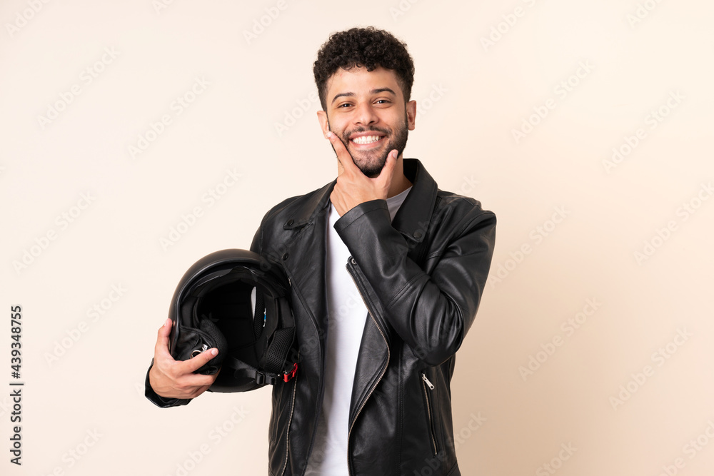 Young Moroccan man with a motorcycle helmet isolated on beige background happy and smiling Young Moroccan man with a motorcycle helmet isolated on beige background happy and smiling