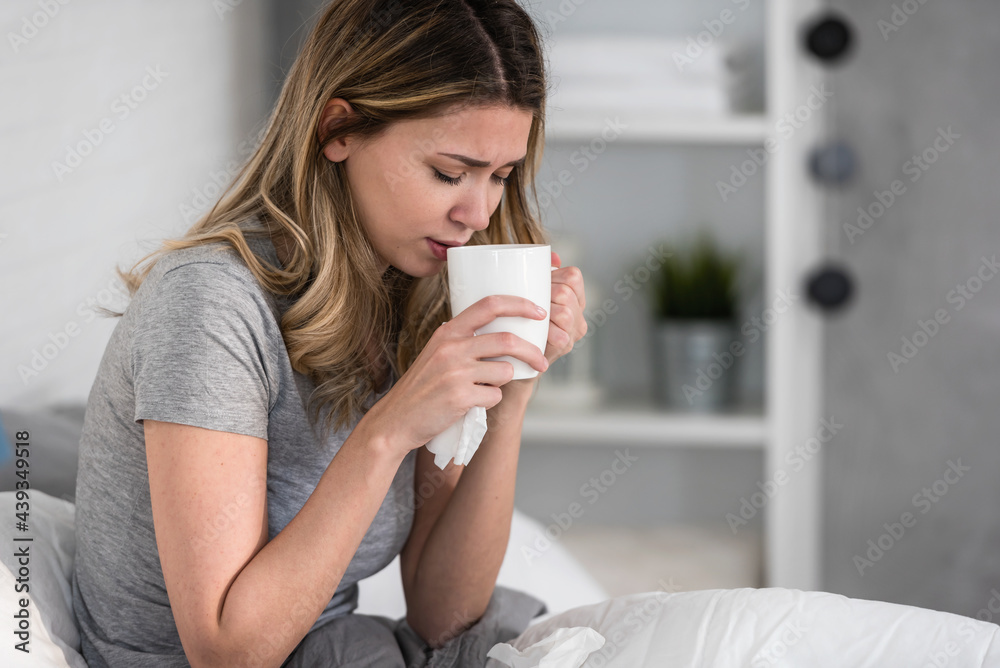 A young pretty girl is sick at home in bed and drinking hot tea