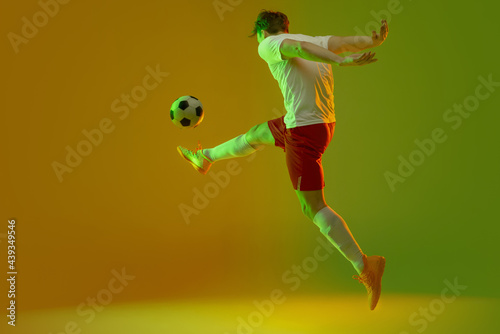 Fototapeta Naklejka Na Ścianę i Meble -  Young caucasian man, male soccer football player training isolated on gradient blue pink background in neon light