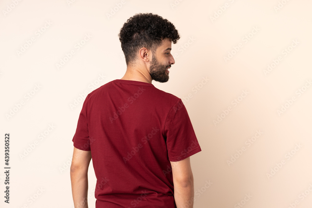 Young Moroccan man isolated on beige background in back position and looking side Young Moroccan man isolated on beige background in back position and looking side