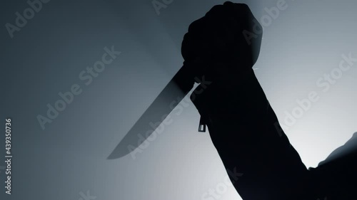 Silhouette man arm holding knife in dark. Criminal hand attacking with dagger.  photo