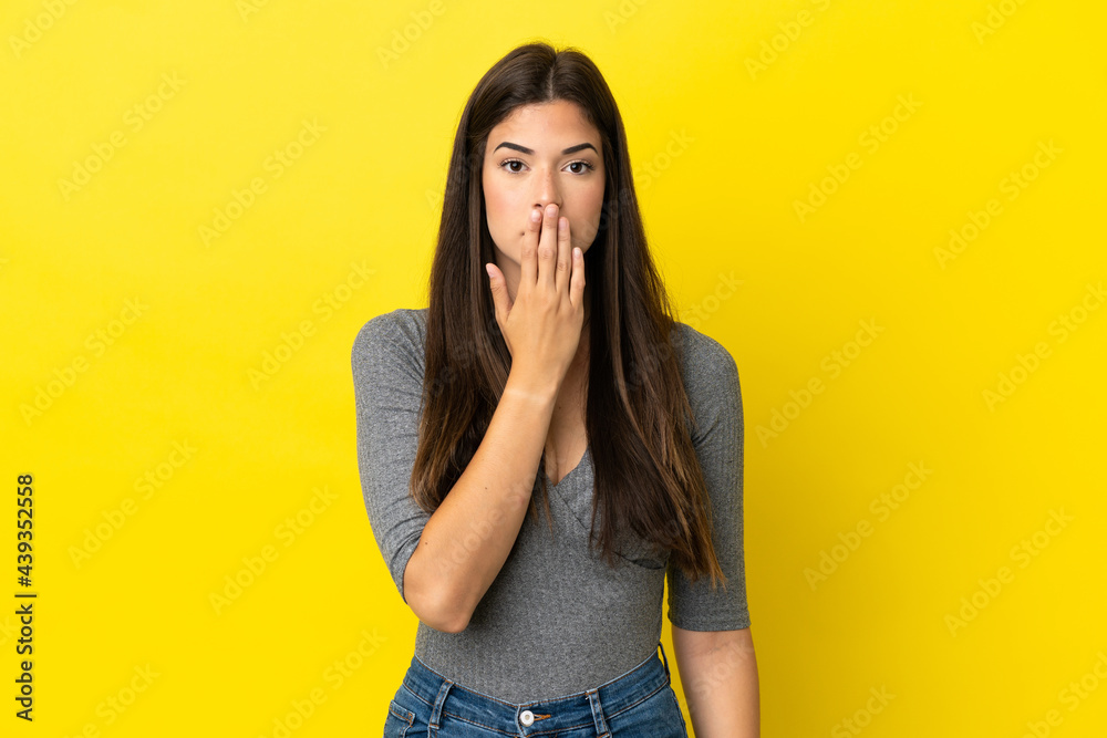 Young Brazilian woman isolated on yellow background covering mouth with hand Young Brazilian woman isolated on yellow background covering mouth with hand