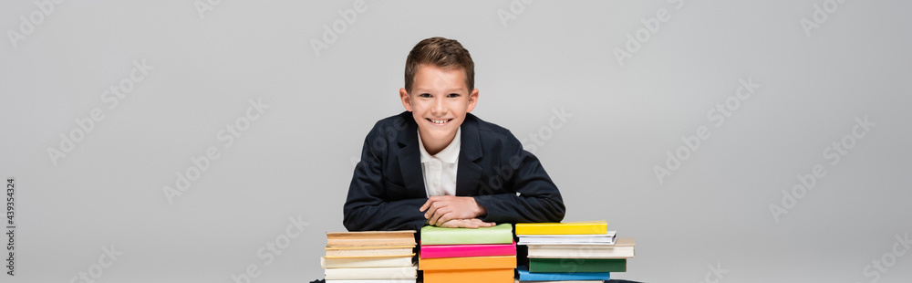 positive schoolboy leaning on pile of books isolated on grey, banner. positive schoolboy leaning on pile of books isolated on grey, banner.