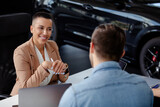 Beautiful smiling car dealer helping young man to buying a new car.