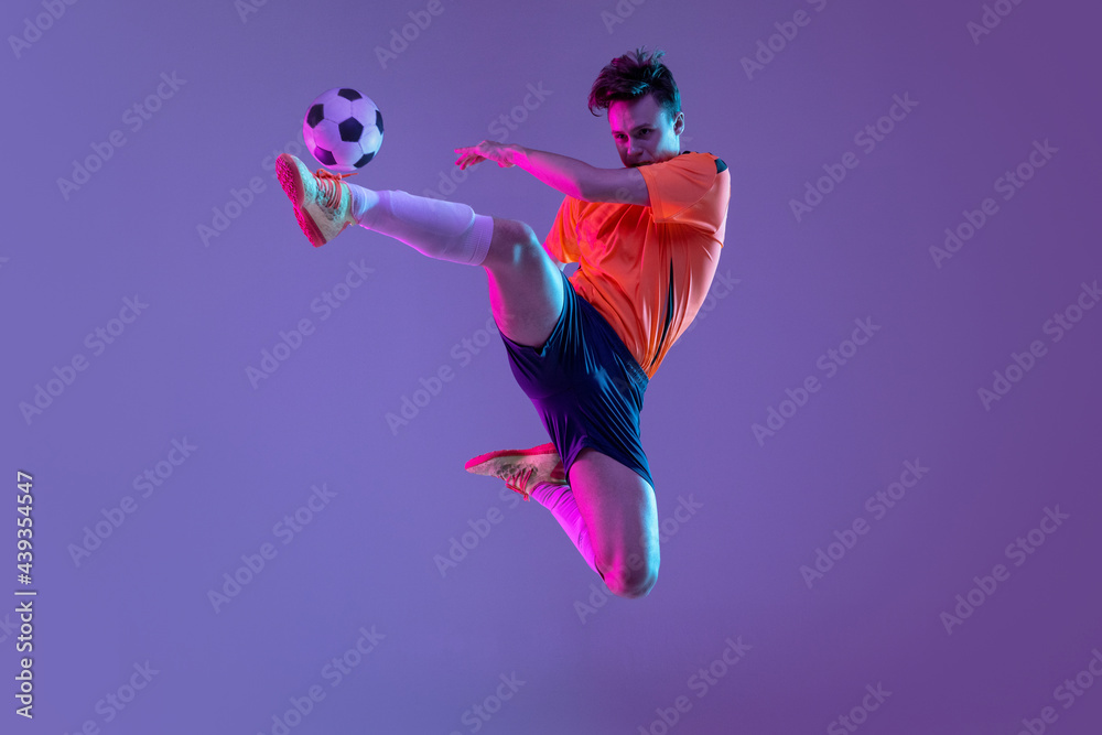 Obraz premium Young caucasian man, male soccer football player training isolated on gradient blue pink background in neon light