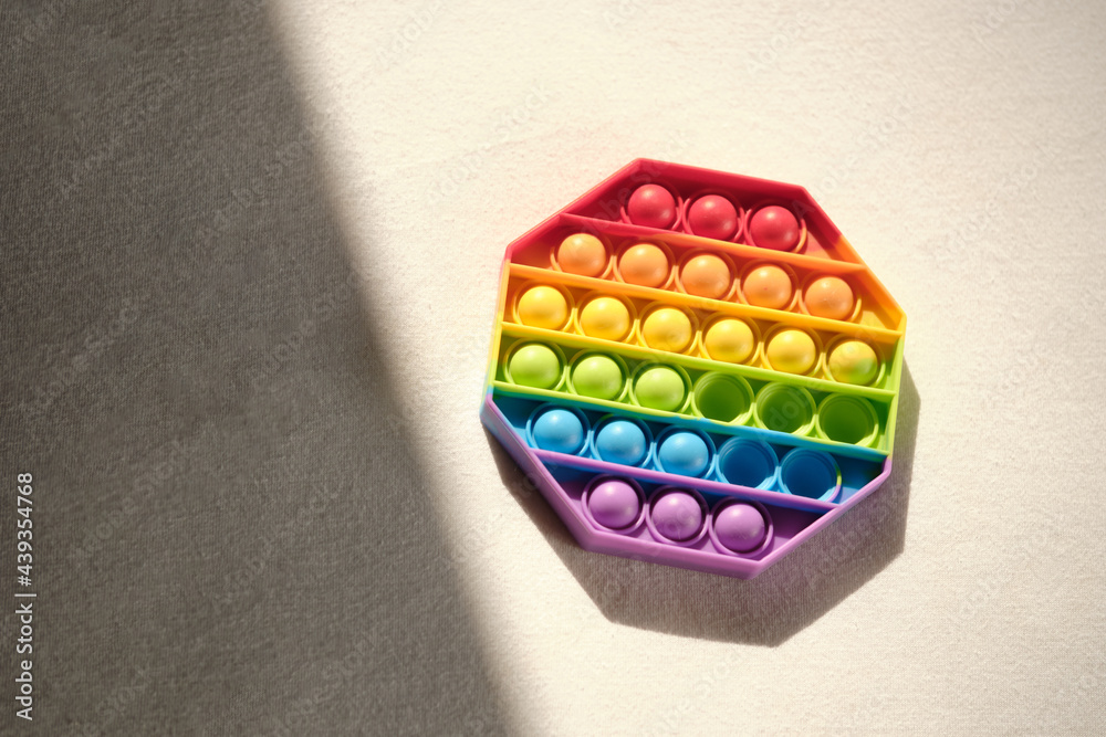 multi-colored plastic toy pop it lies on the bed in bright sunlight. playing at home during summer holidays multi-colored plastic toy pop it lies on the bed in bright sunlight. playing at home during summer holidays