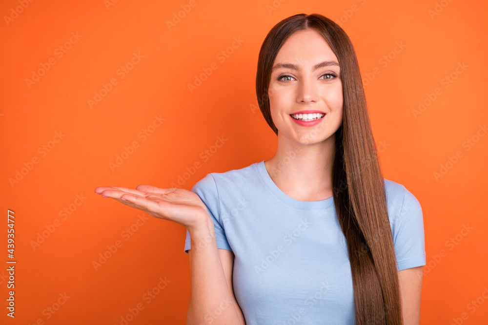 Photo of pretty long hairdo millennial lady hold empty space wear blue t-shirt isolated on orange color background Photo of pretty long hairdo millennial lady hold empty space wear blue t-shirt isolated on orange color background