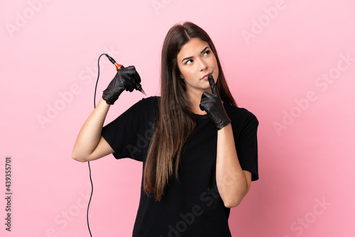 Tattoo artist woman isolated on pink background having doubts while looking up