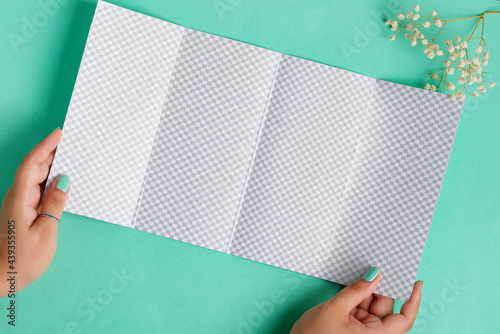 Four-fold brochure mockup in a hand above aquamarine background