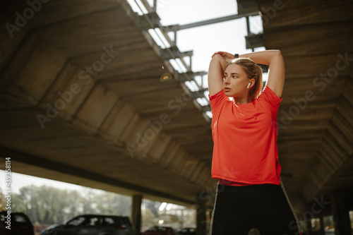 Portrait of fit and sporty young woman doing stretching under the bridge.
