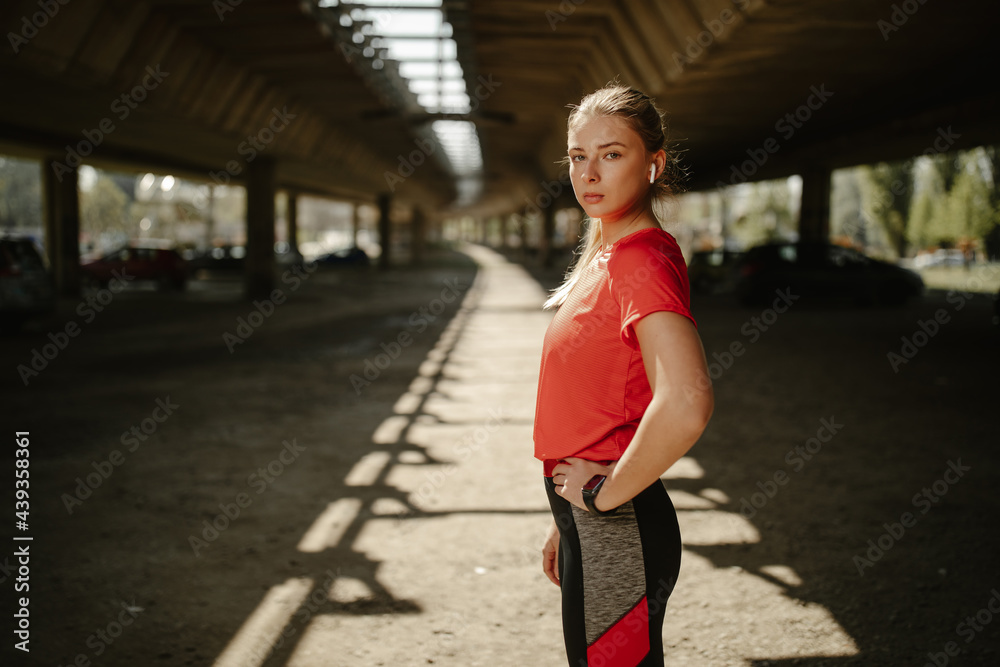 Athlete looking at camera and holding hand on hips. Motivated and focused sporty woman before a run. Athlete looking at camera and holding hand on hips. Motivated and focused sporty woman before a run.