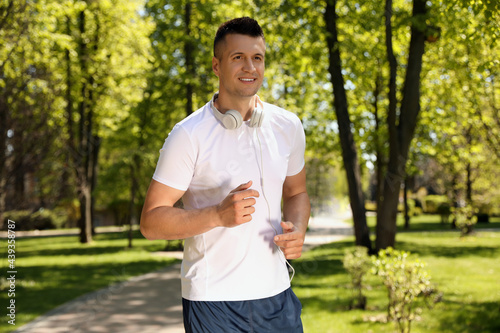 Young man with headphones on morning run in park. Fitness lifestyle