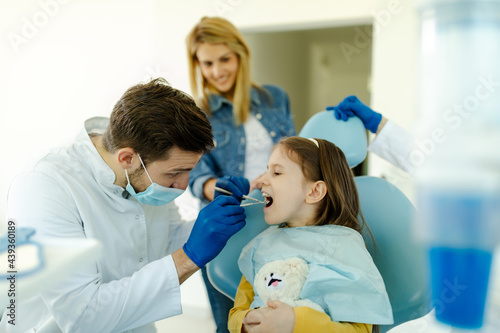 Male doctor with instruments in the hands looking girls teeth.