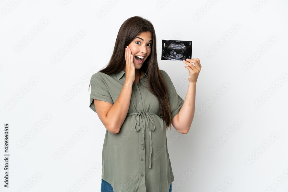 Young Brazilian woman isolated on white background pregnant and surprised while holding an ultrasound Young Brazilian woman isolated on white background pregnant and surprised while holding an ultrasound