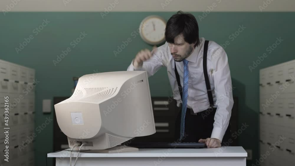 Angry man is destroying old computer with baseball bat in office.