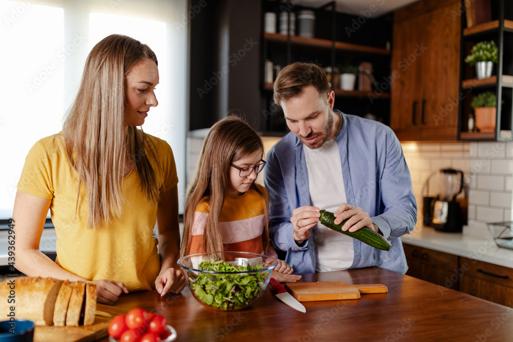 Handsome man, attractive young woman and their cute little daughter are making salad together.
