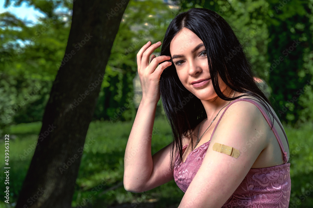 Smiling female with band-aid on arm after vaccination.. Woman feeling positive after getting vaccinae. Happy teenage girl outdoor Smiling female with band-aid on arm after vaccination.. Woman feeling positive after getting vaccinae. Happy teenage girl outdoor