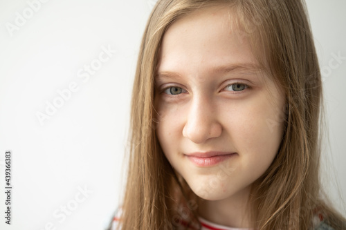 portrait of beautiful teenage girl with long hair smiling standing against white wall