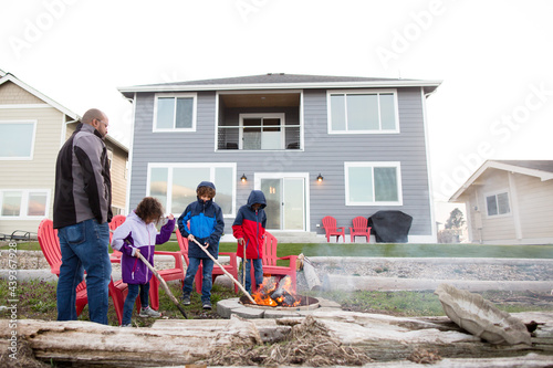 Father and children tend smoky campfire in backyard