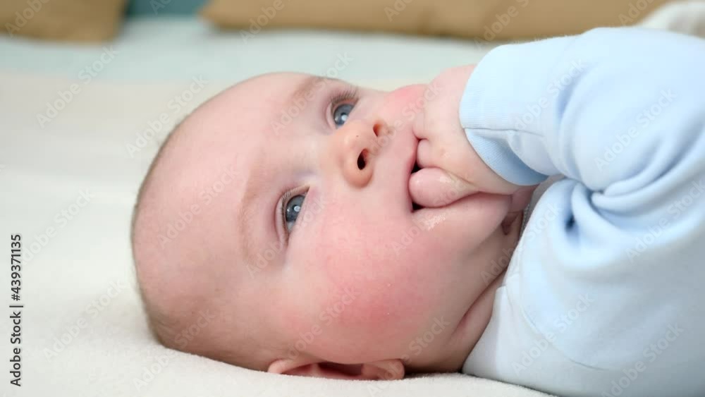Portrait of adorable baby boy with blue eyes sucking his hand while lying on bed. Portrait of adorable baby boy with blue eyes sucking his hand while lying on bed.