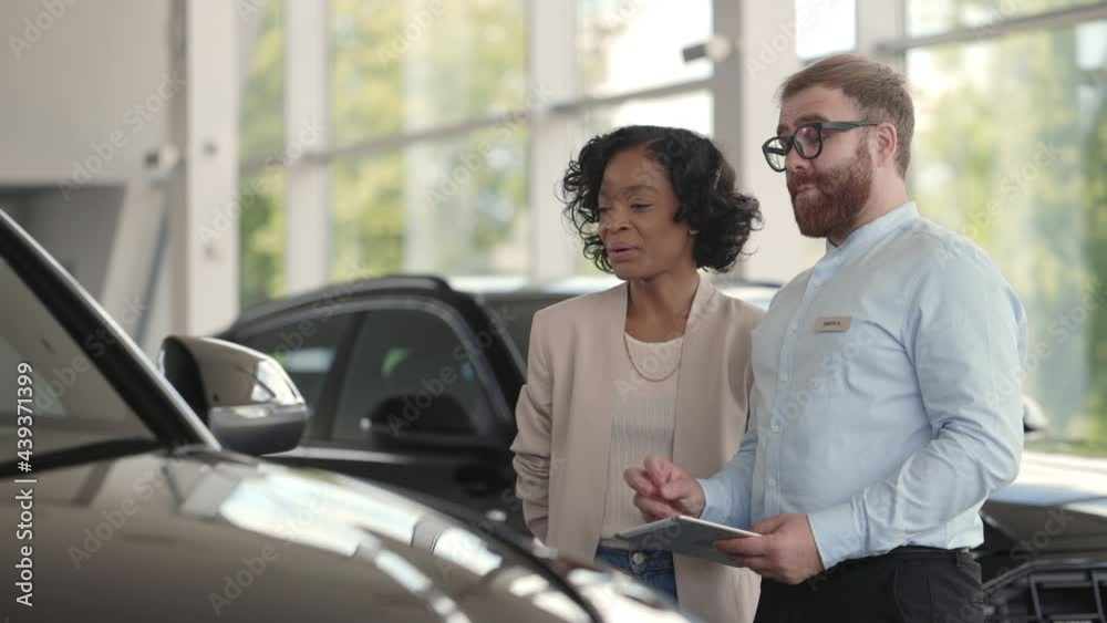 Male dealer using tablet while presenting car to customer Male dealer using tablet while presenting car to customer