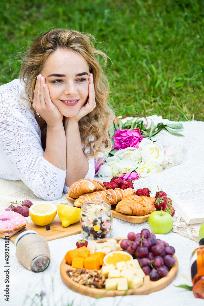 Beautiful woman resting in park sitting on a picnic blanket with fruits and wine. 