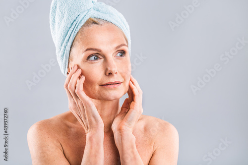 Portrait of smiling senior woman feeling soft skin with hand after spa bath. Mature woman draped in towel looking at camera. Lady in bathrobe after shower isolated over white background.