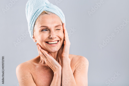 Portrait of smiling senior woman feeling soft skin with hand after spa bath. Mature woman draped in towel hair looking at camera. Lady in bathrobe after shower isolated over white background.