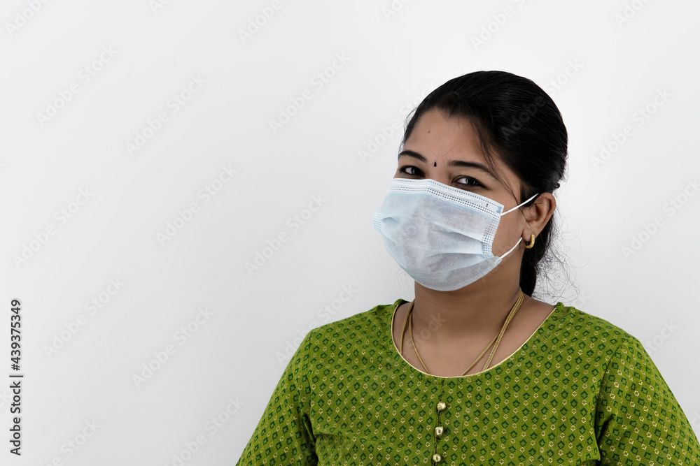 Beautiful smiling Indian young woman in protective face mask, happy female in medical facial cover from COVID-19 thinking, healthcare concept, isolated over white background with space at left.. Beautiful smiling Indian young woman in protective face mask, happy female in medical facial cover from COVID-19 thinking, healthcare concept, isolated over white background with space at left..