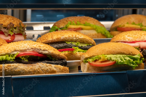 Group of different sandwiches made from sesame buns with various type of meat  vegetables and salads lies on shelf. Side view. Buffet and catering service theme.