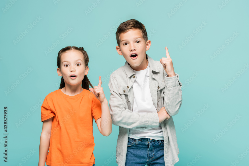 excited kids pointing up with fingers while having idea isolated on blue. excited kids pointing up with fingers while having idea isolated on blue.