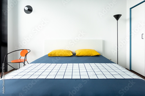 Blue and white bedroom with brown floor, yellow pillows and an orange chair. Frontal view photo